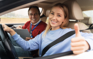 Smiling woman in car with instructor giving thumbs up.